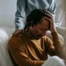 sorrowful black man touching head in dismay near supporting wife