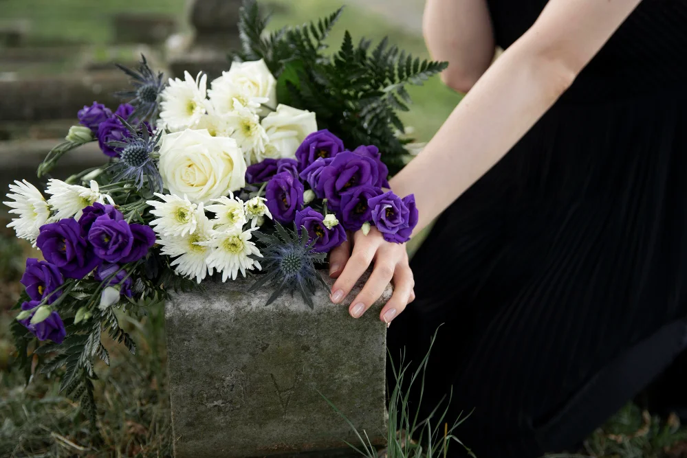 woman putting white and purple flowers on grave